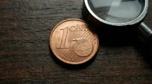 Moneta da 1 centesimo su tavolo in legno accanto a una lente d'ingrandimento