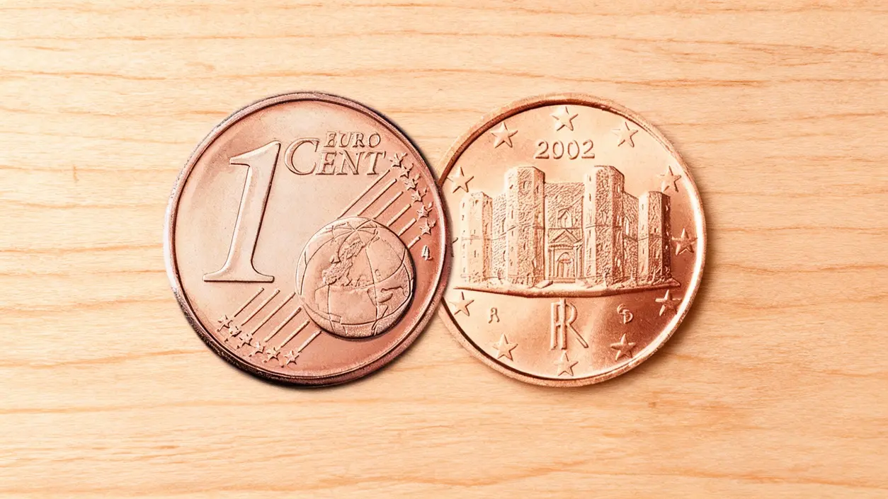 Due monete italiane da 1 centesimo ed euro su sfondo in legno chiaro