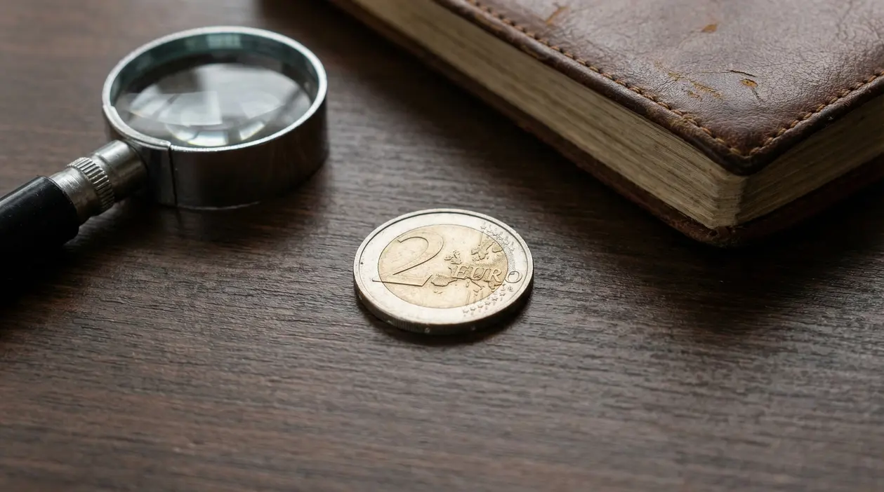 Moneta da 2 euro su tavolo in legno con lente d'ingrandimento e libro antico