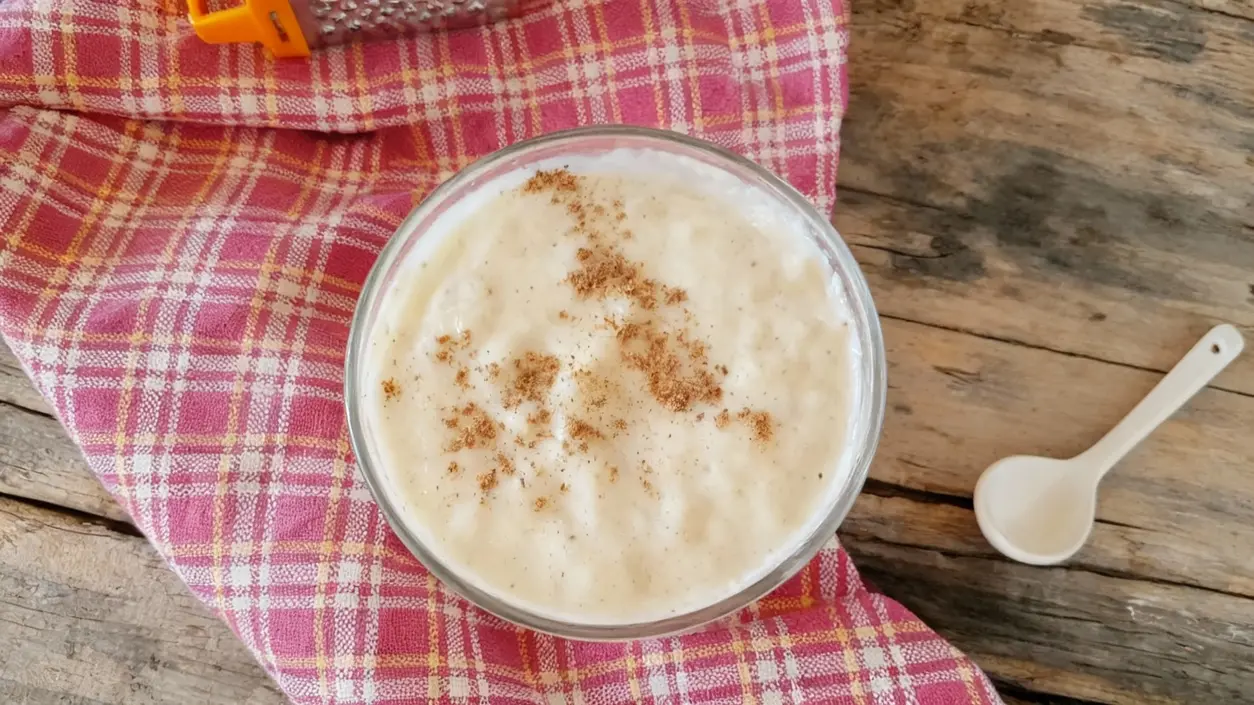 Ciotola di besciamella leggera con spolverata di noce moscata su tovagliolo a quadretti