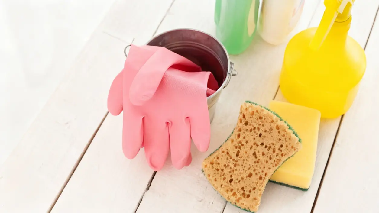 Guanti rosa, spugne e flaconi spray per la pulizia su un tavolo bianco