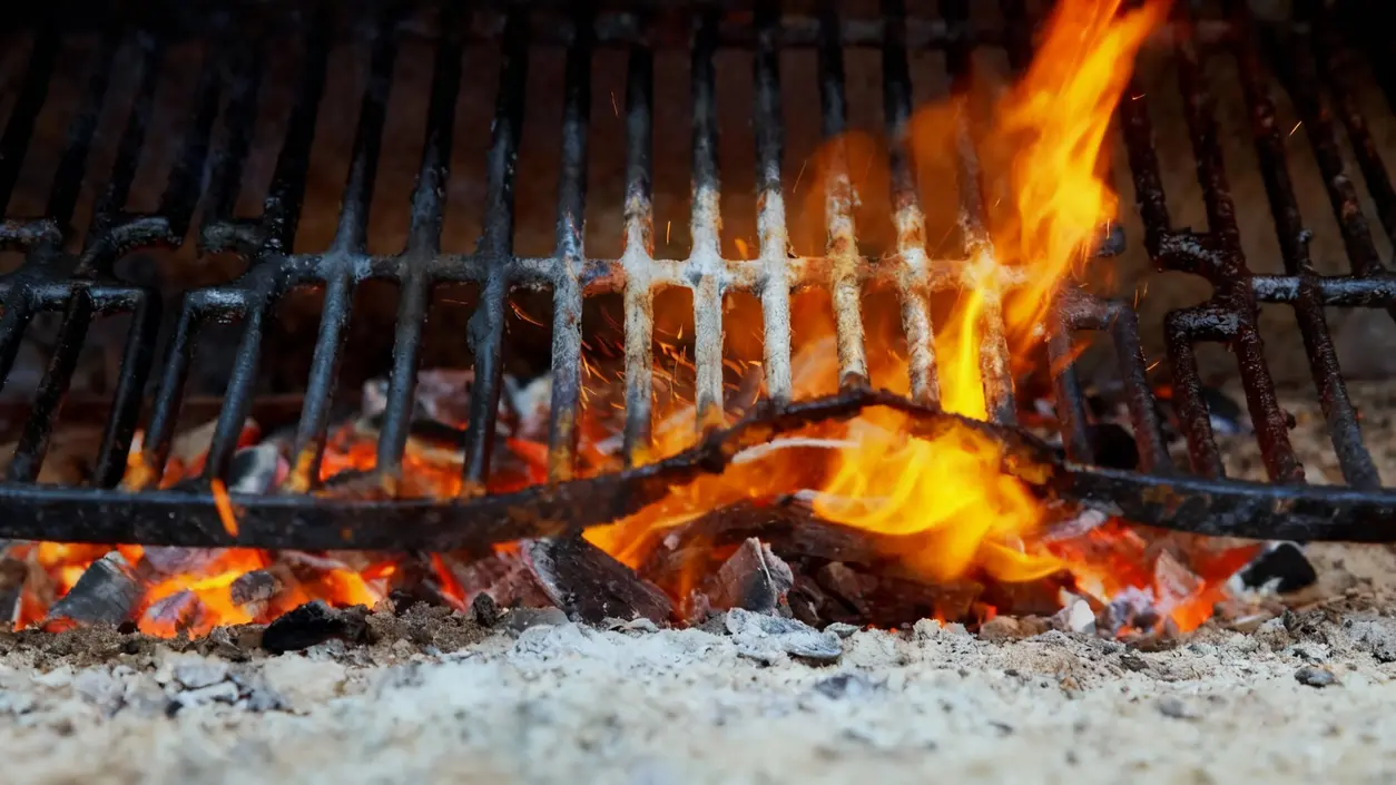 Griglia da barbecue incrostata posta sopra braci e fiamme accese
