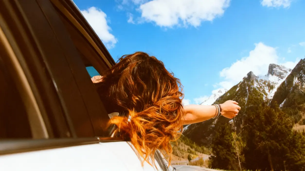 Una persona con il braccio fuori dal finestrino di un'auto, in viaggio tra le montagne