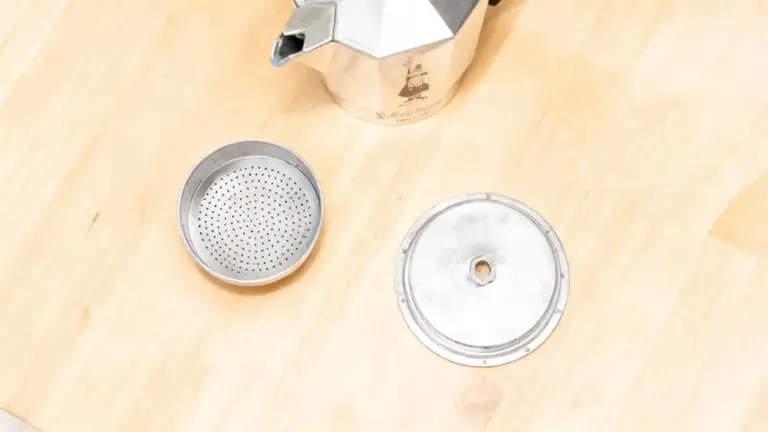 Componenti smontati di una moka su un piano in legno chiaro