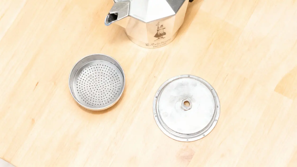 Componenti smontati di una moka su un piano in legno chiaro