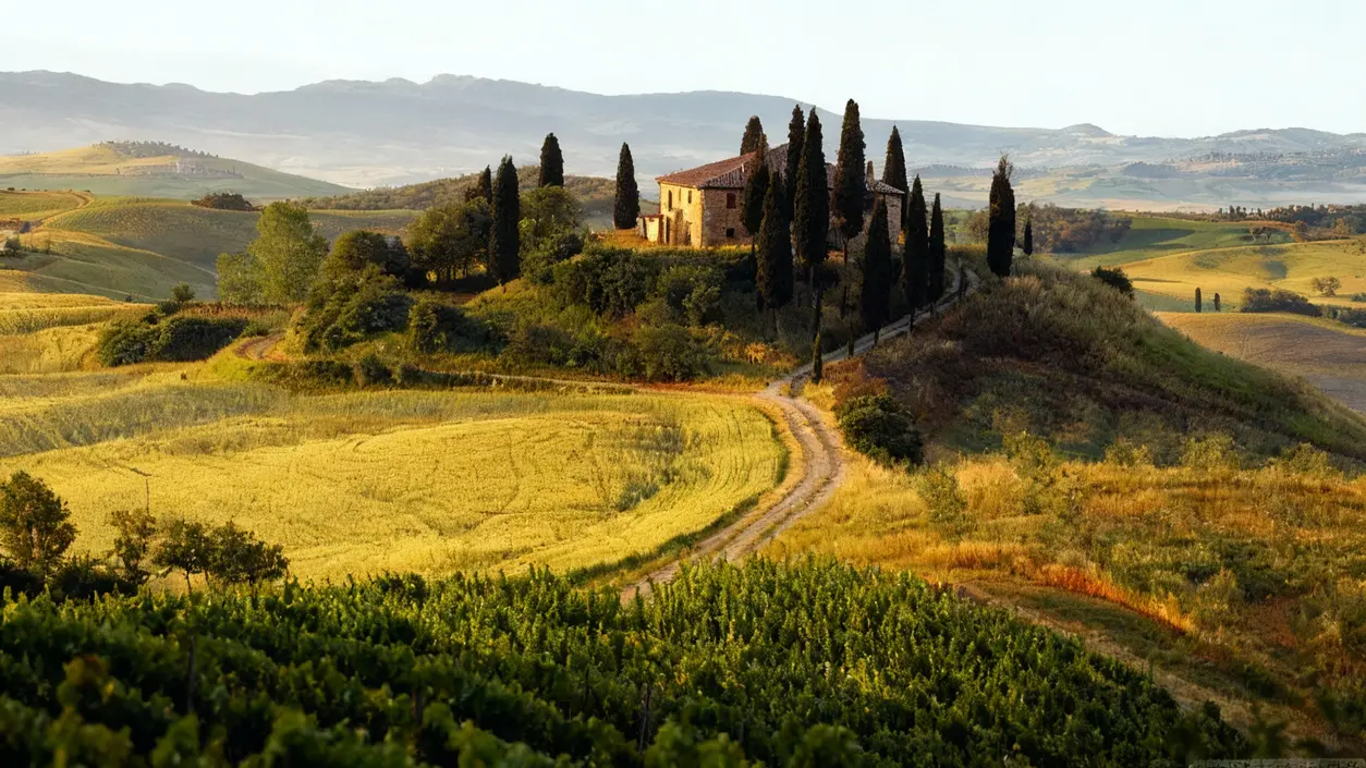 Casale in pietra circondato da cipressi e campi nella campagna toscana al tramonto