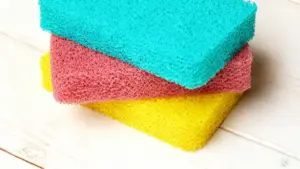 Tre spugne colorate per i piatti sovrapposte su un piano di legno chiaro