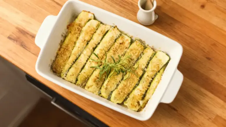 Zucchine gratinate al forno disposte in una teglia bianca su un tavolo di legno