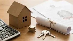 Modellino di casa, calcolatrice, monete, chiavi e documenti su un tavolo