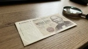 Banconota da 1.000 lire con il ritratto di Garibaldi appoggiata su un tavolo accanto a una lente d'ingrandimento