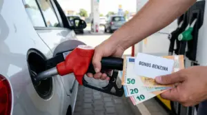 Una persona fa rifornimento a un'auto con banconote e una tessera con scritto Bonus Benzina in mano