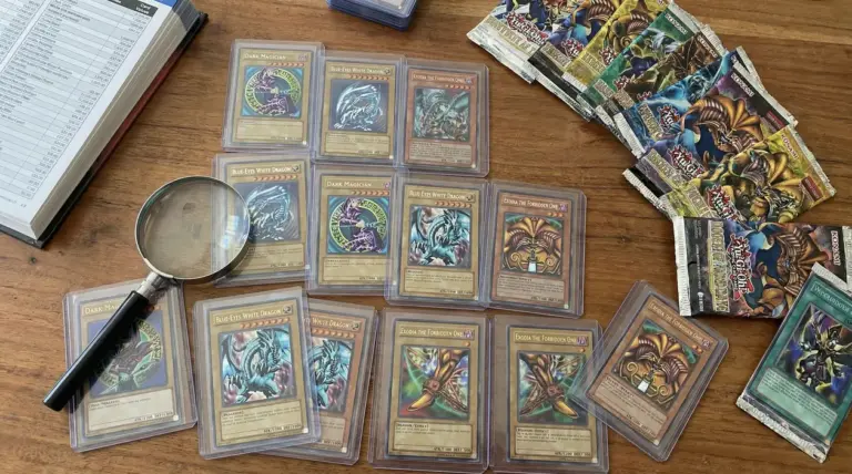 Carte rare di Yu-Gi-Oh! protette in custodie su un tavolo con una lente d'ingrandimento e bustine non aperte.
