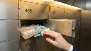 Mano che ripone mazzette di banconote in euro in una cassetta di sicurezza bancaria