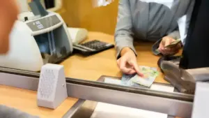 Impiegato allo sportello di una banca mentre conta delle banconote dietro un vetro protettivo