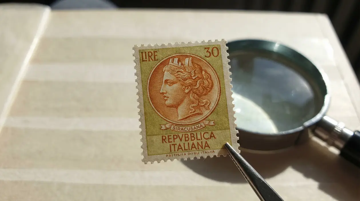 Francobollo italiano da 30 lire della serie Siracusana tenuto con pinzette sopra un album.