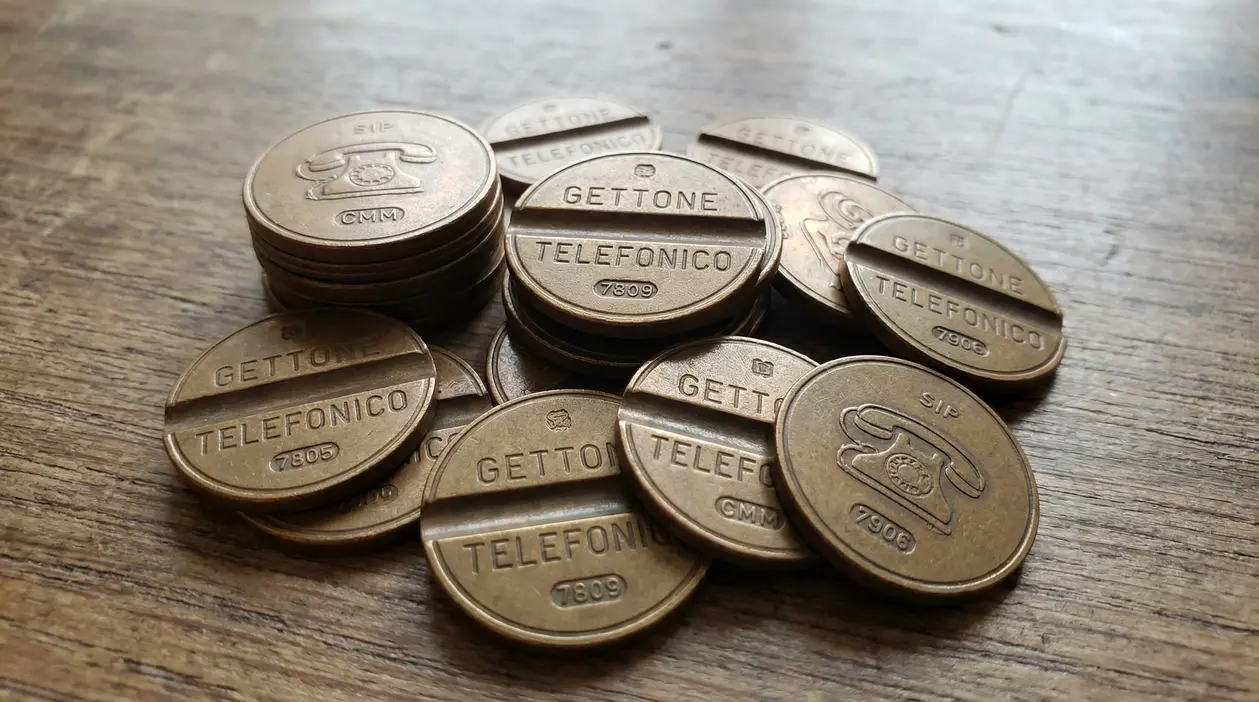 Gettoni telefonici italiani in metallo degli anni ’60 e ’70 su un tavolo in legno