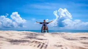 Una persona in sedia a rotelle con le braccia aperte su una spiaggia soleggiata