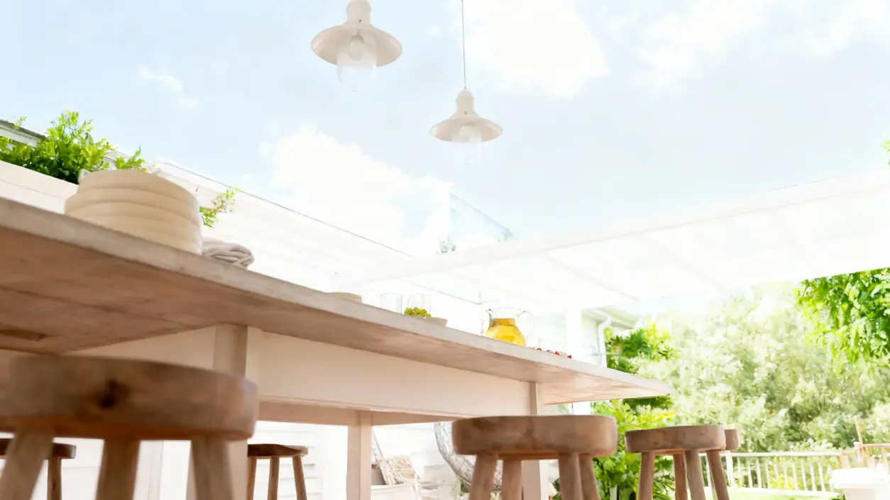 Tavolo in legno sotto una veranda luminosa con sedie e stoviglie