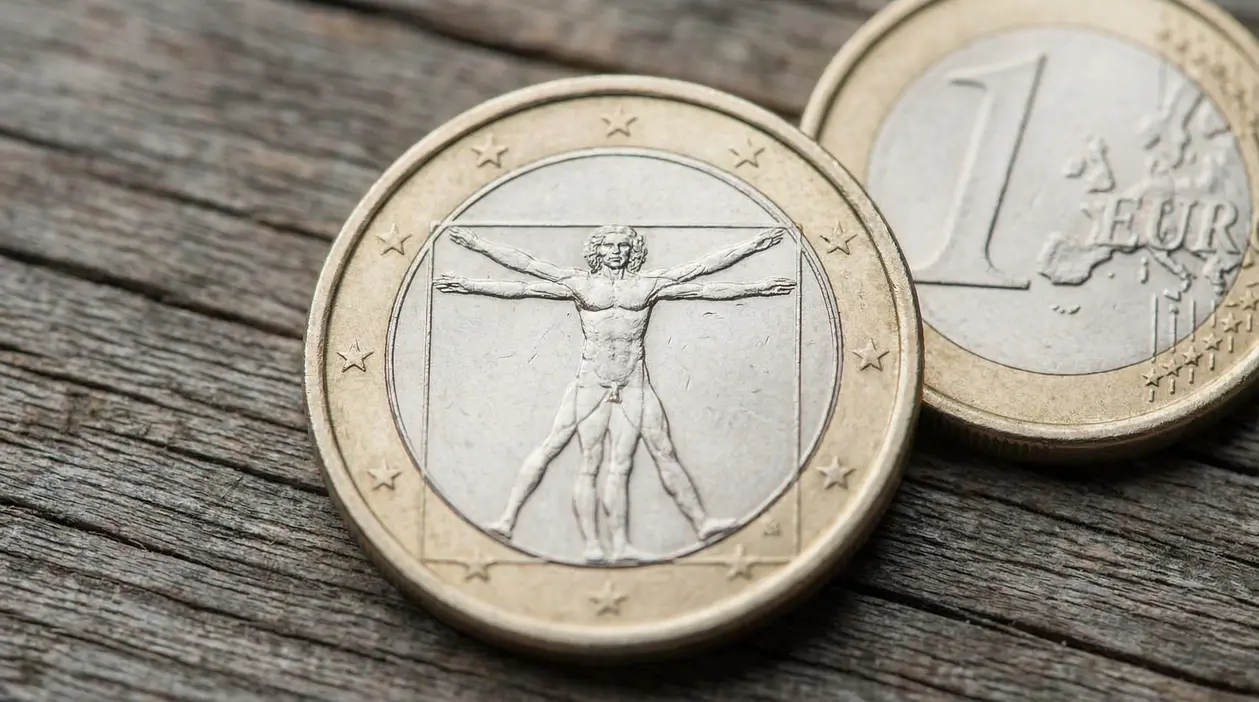Monete da 1 euro su superficie in legno, in primo piano una con l'Uomo Vitruviano