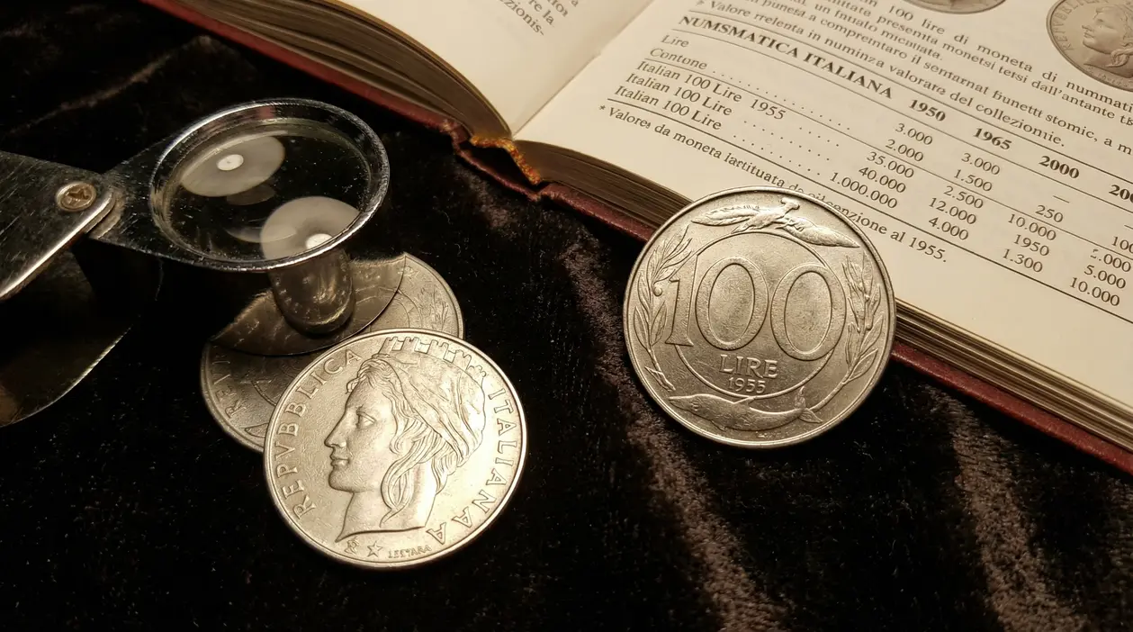 Monete italiane da 100 lire con lente d'ingrandimento e catalogo numismatico