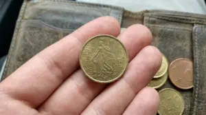 Una mano tiene una moneta da 10 centesimi di euro davanti a un portafoglio in pelle