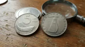 Monete da 5 lire italiane con delfino e timone su superficie di legno