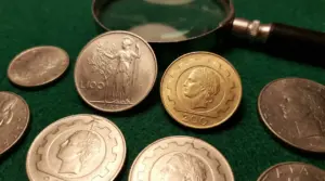 Monete da 100 e 200 lire italiane su un tavolo verde con una lente d'ingrandimento