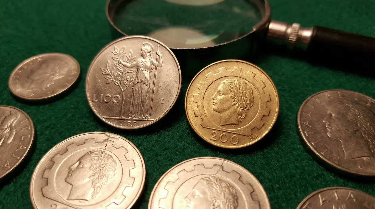 Monete da 100 e 200 lire italiane su un tavolo verde con una lente d'ingrandimento