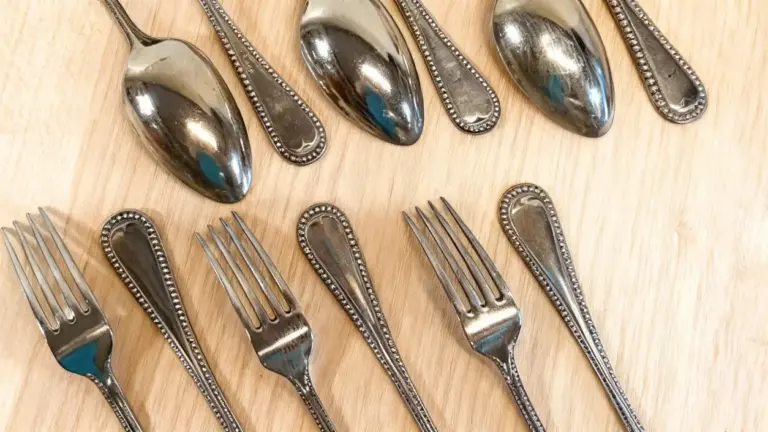 Vecchie posate in alpacca disposte su un tavolo di legno chiaro