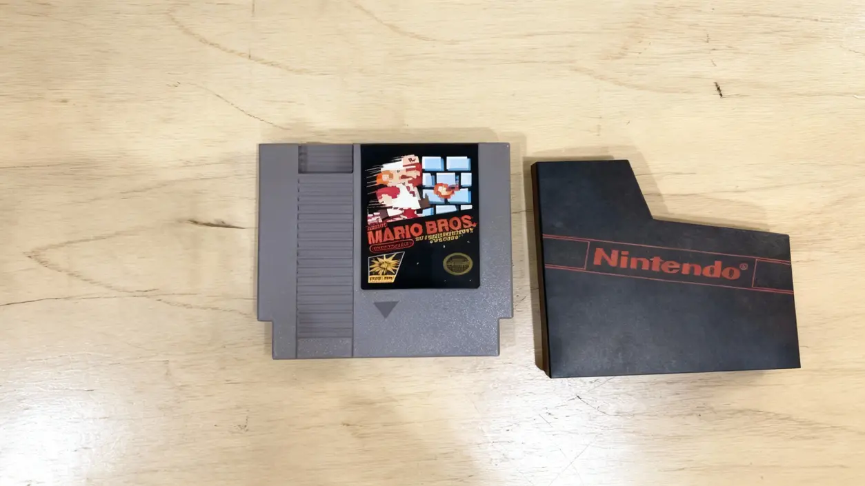 Cartuccia vintage di videogame su un tavolo di legno chiaro con custodia nera accanto