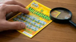 Mano che gratta un biglietto gratta e vinci su un tavolo con una lente di ingrandimento accanto