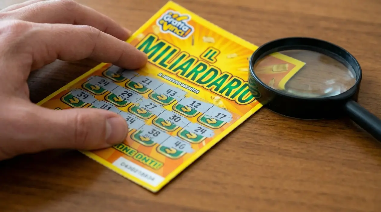 Mano che gratta un biglietto gratta e vinci su un tavolo con una lente di ingrandimento accanto