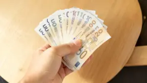 Persona che tiene in mano una serie di banconote in euro sopra un tavolo di legno
