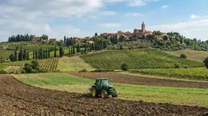 Trattore al lavoro in un terreno agricolo con un borgo collinare sullo sfondo
