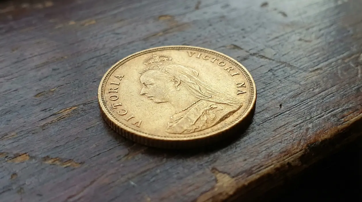 Vecchia moneta d’oro britannica con profilo di regina su superficie in legno