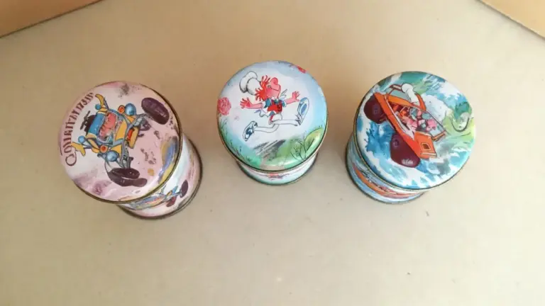 Tre vecchi barattoli in latta illustrata con disegni colorati su sfondo neutro