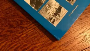 Copertina parziale di un libro blu con foto in bianco e nero su un tavolo in legno